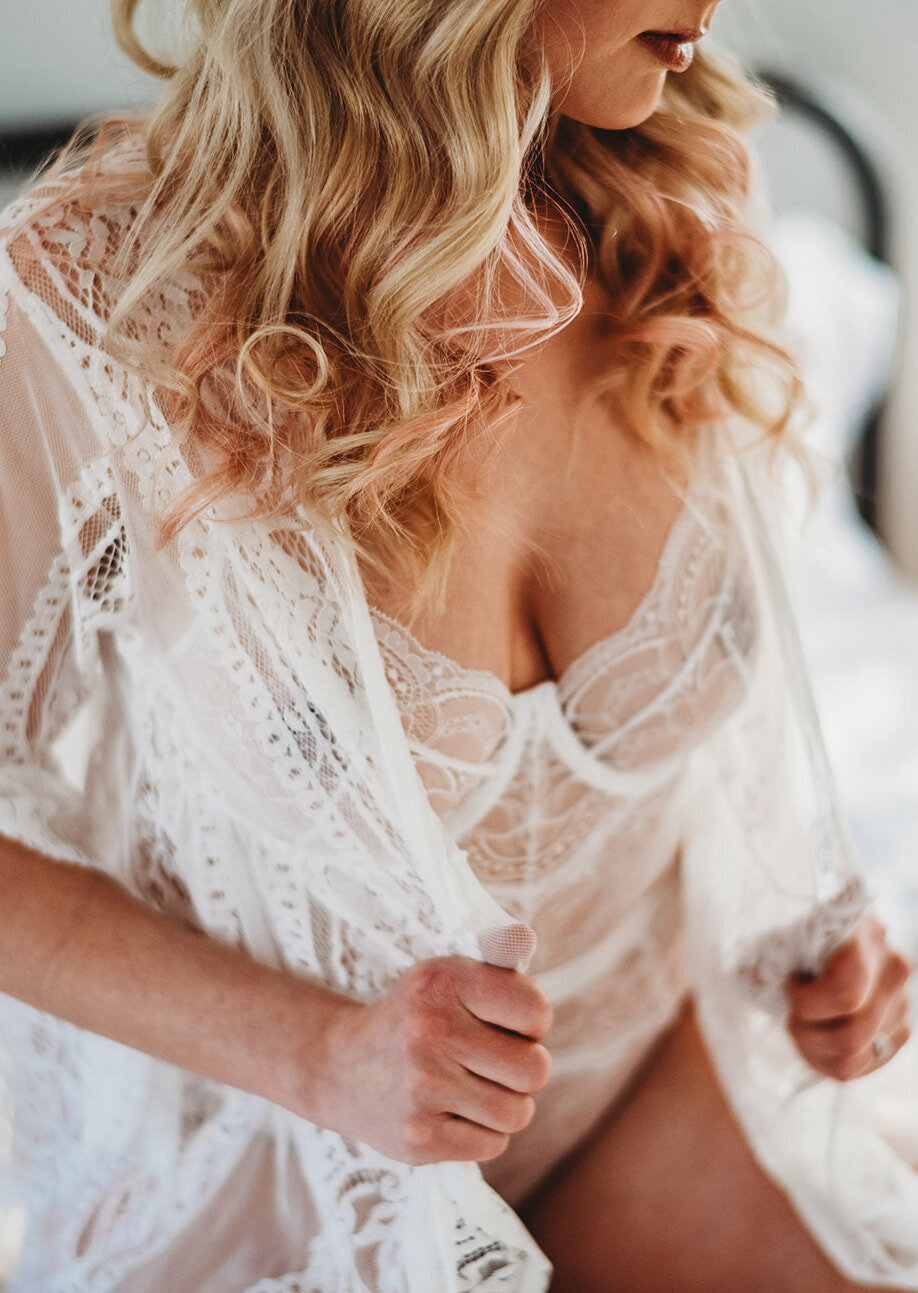 Baltimore photographers  captures bridal boudiors with woman in a lace one piece lingerie sitting on a bed while holding a lace robe