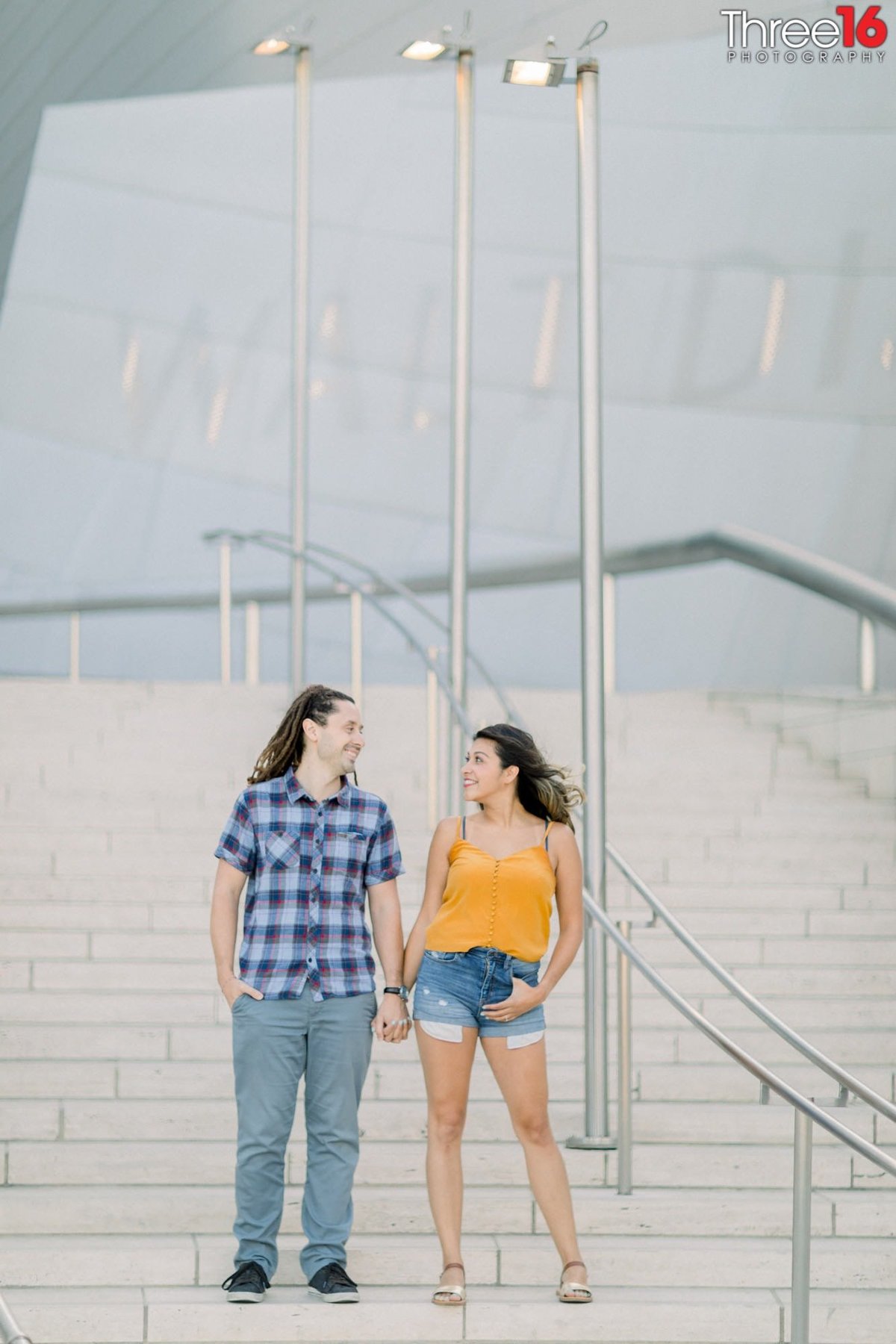 Engaged couple hold hands on the steps of the Walt Disney Concert Hall