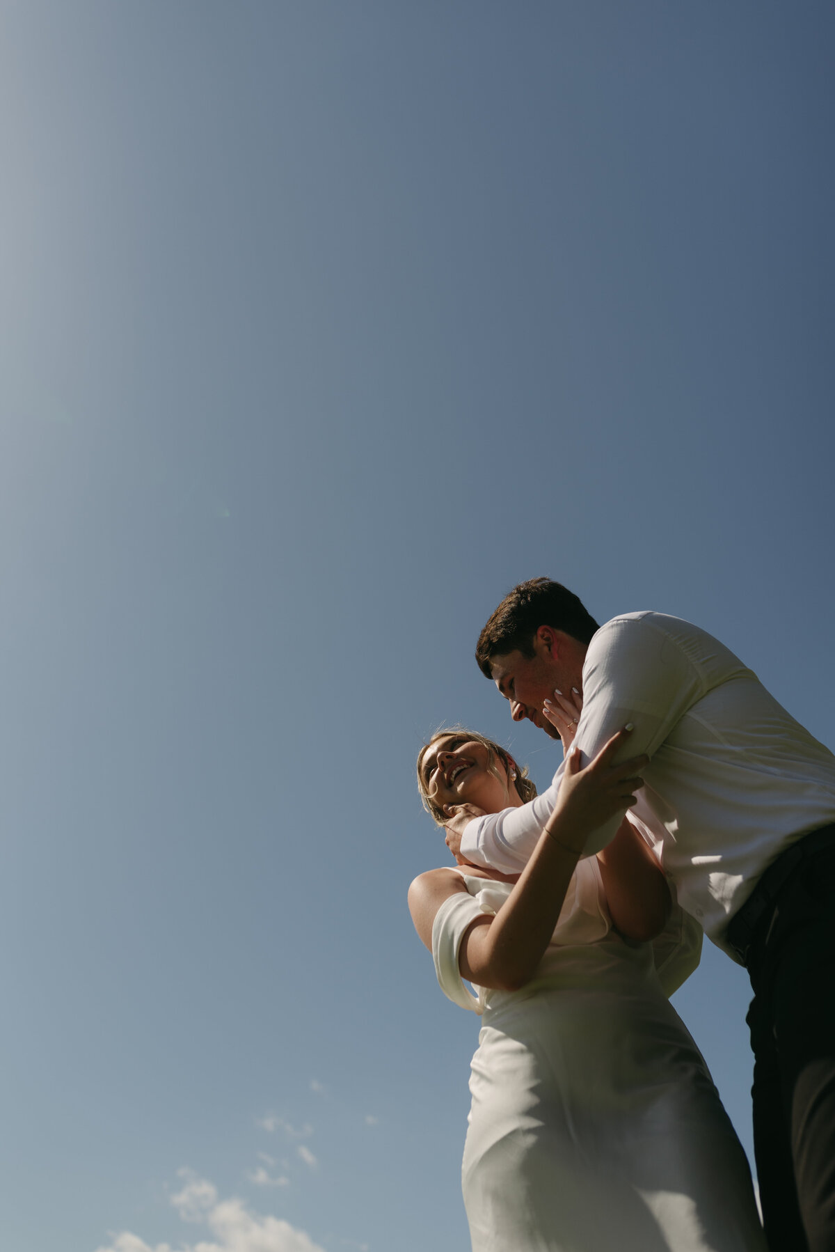 A wedding couple laughing and holding eachother close with the golden hour blue sky above them. 
