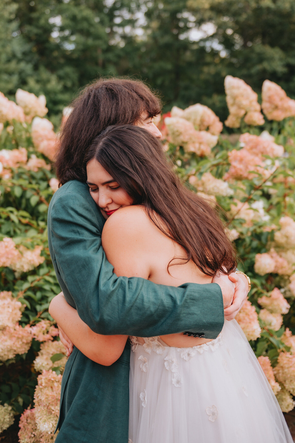A couple hugs one another in front of flowers
