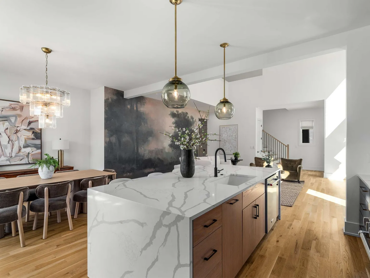 Open-concept kitchen with waterfall island, glass pendants, scenic mural, and designer dining area blending seamlessly into a cozy living room