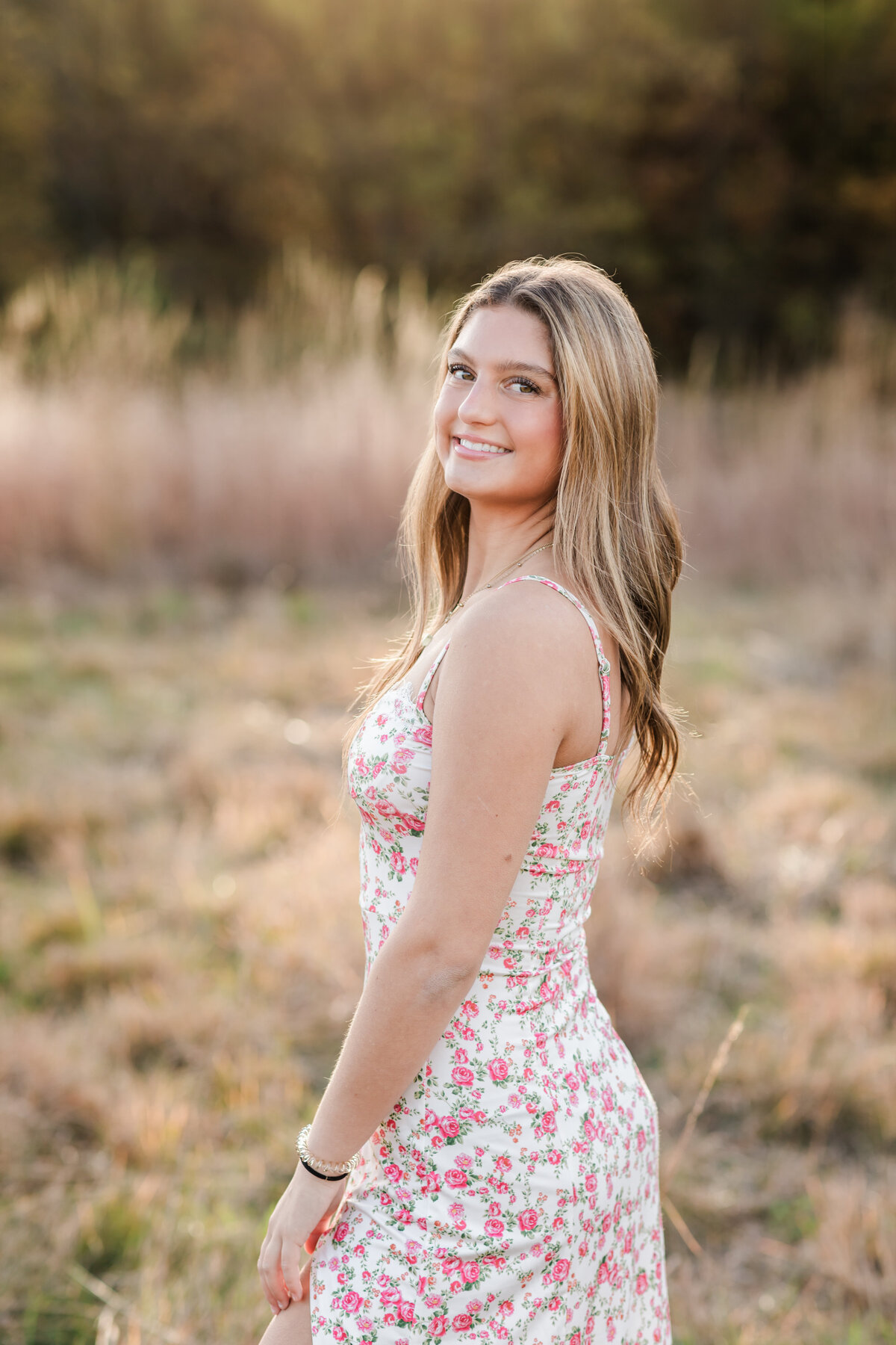 senior girl in floral dress posing for senior photos in field at Westcreek Reservation in Parma, Ohio 