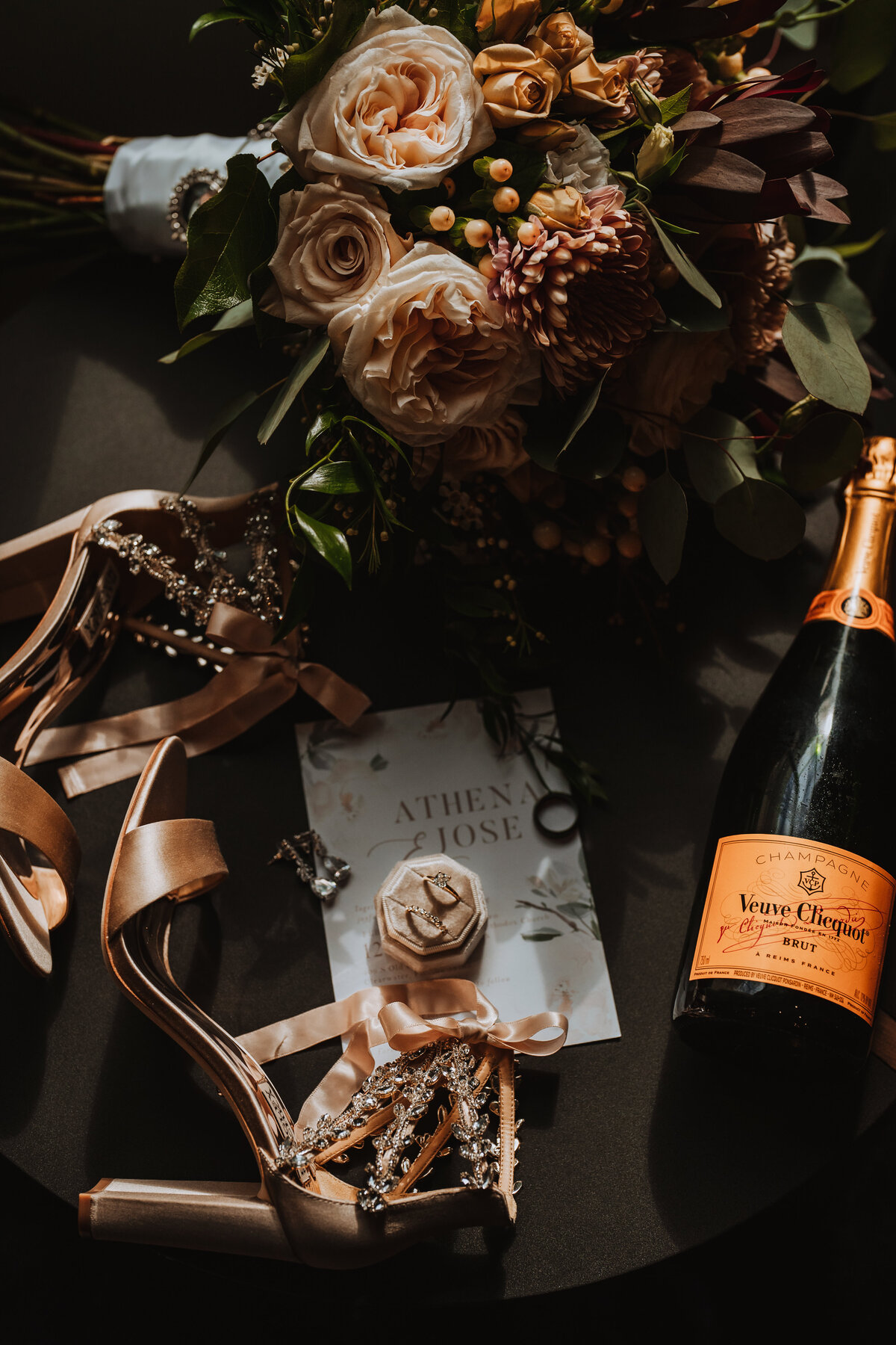 Photo of brides wedding details including rings shoes invitation and champagne bottle of veuve clicquot