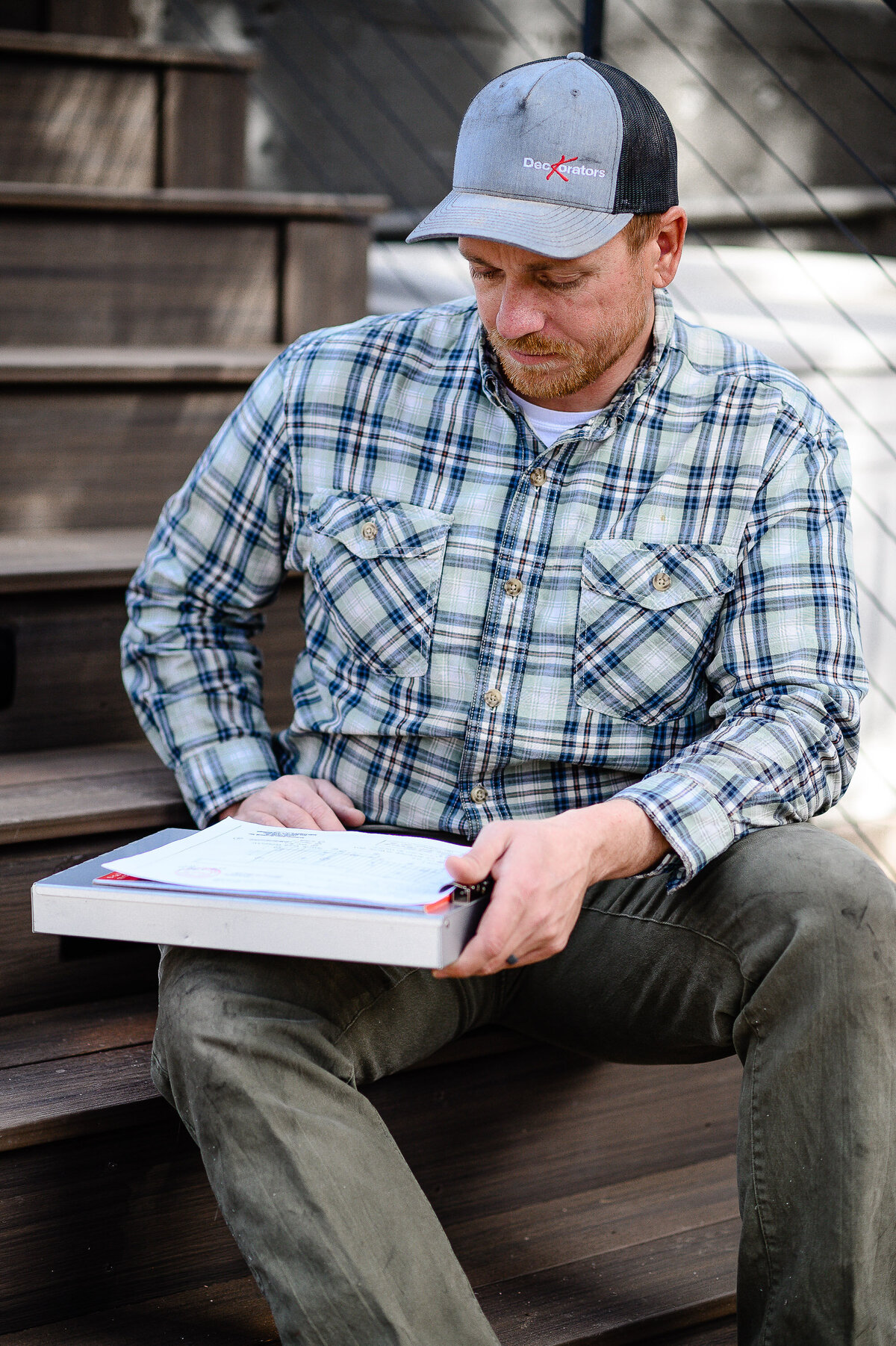 brand images of a man in a flannel  shirt looking at a folder with papers while sitting on stairs