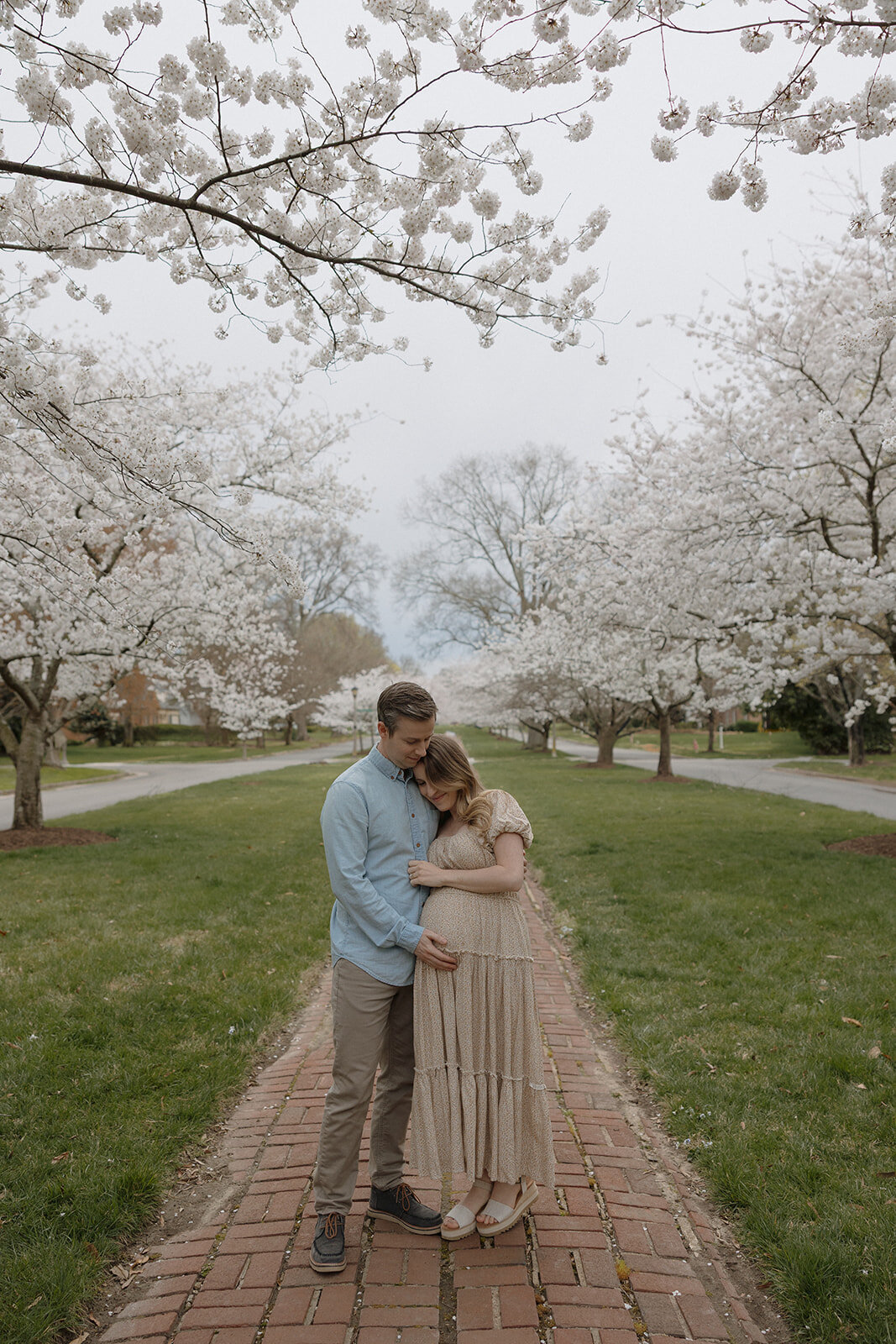 couple hugging during maternity photoshoot surrounded by cherry blossoms during session with RVA maternity photographer