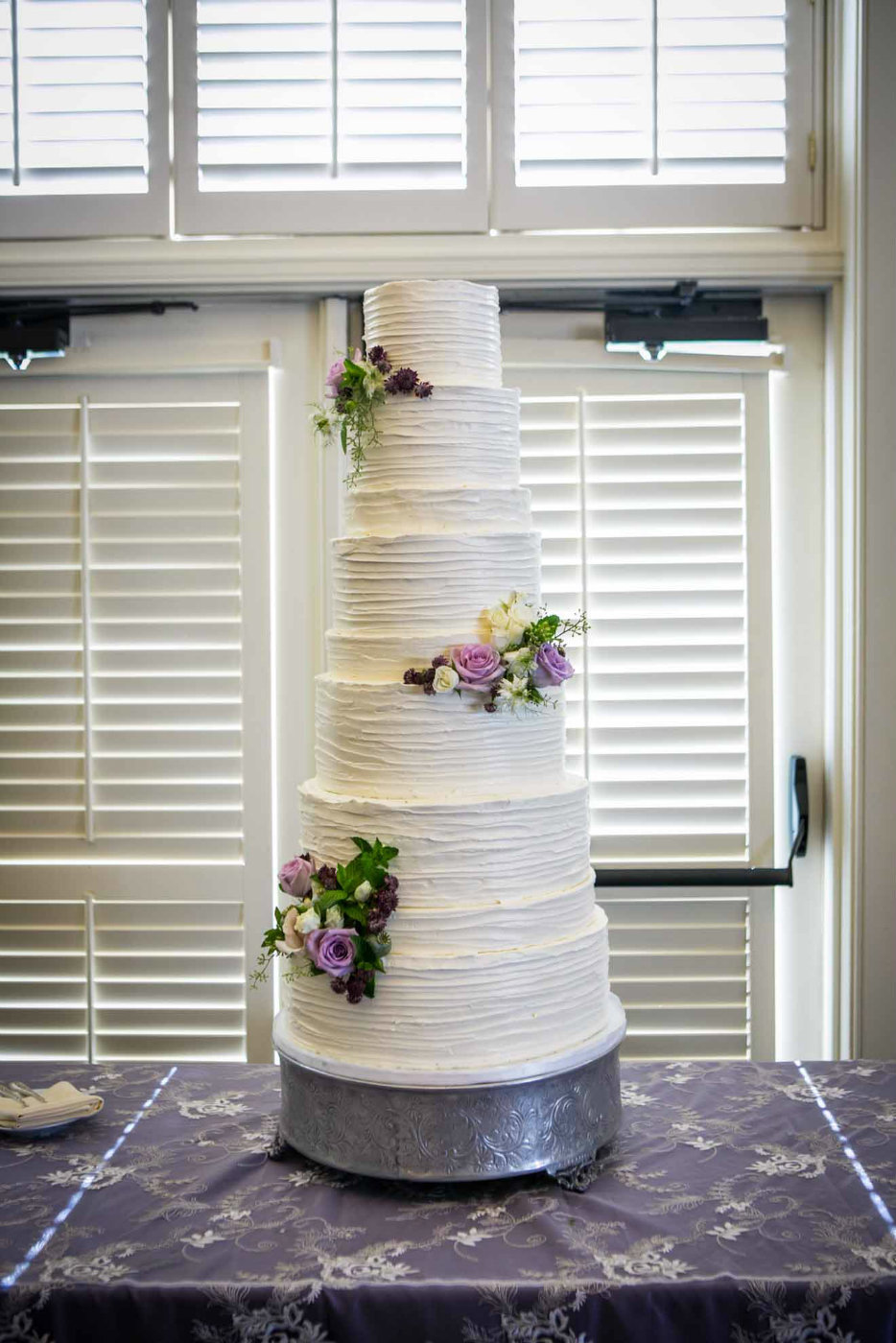 tall white wedding cake with fresh purple flowers