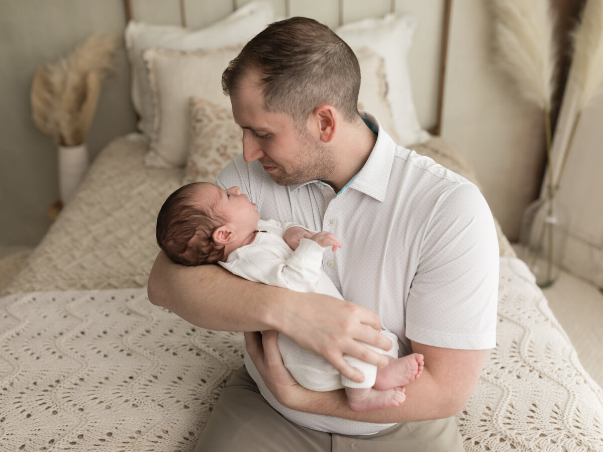 dad holding newborn baby boy in white onesie for studio lifestyle session 