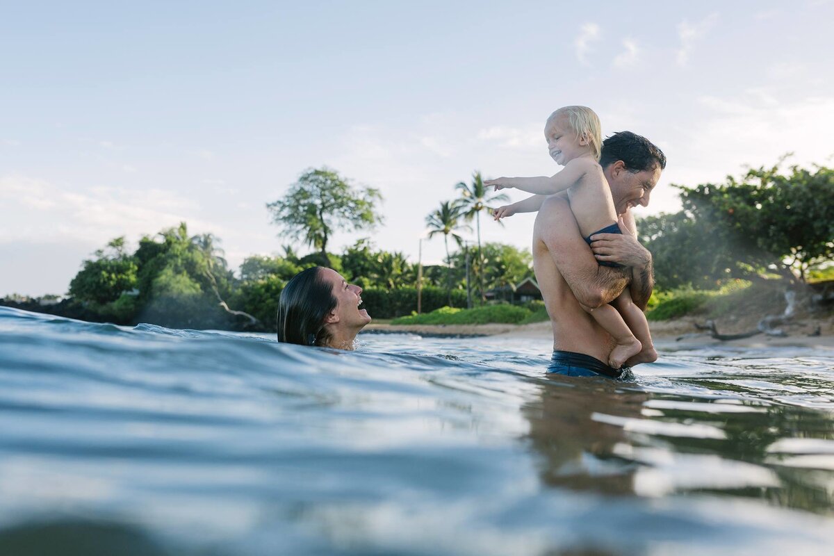 Shawn and Adam play in the water among the palm trees with one of their children during a family photoshoot