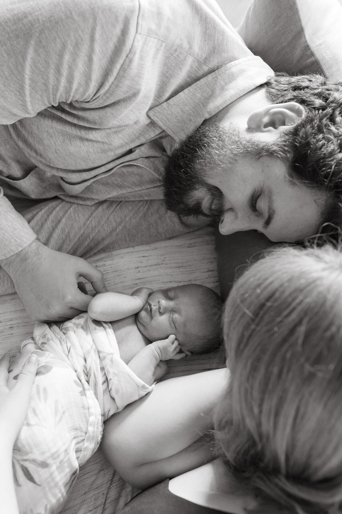 Black and white image of dad and newborn laying down together. Newborn photography capturing tender family moments.