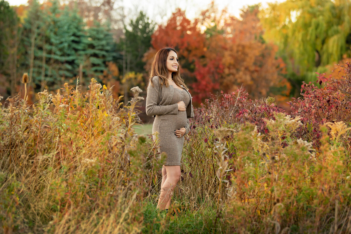 woman wearing a beige dress holding her belly for her outdoor fall maternity photography session in Burlington, Ontario