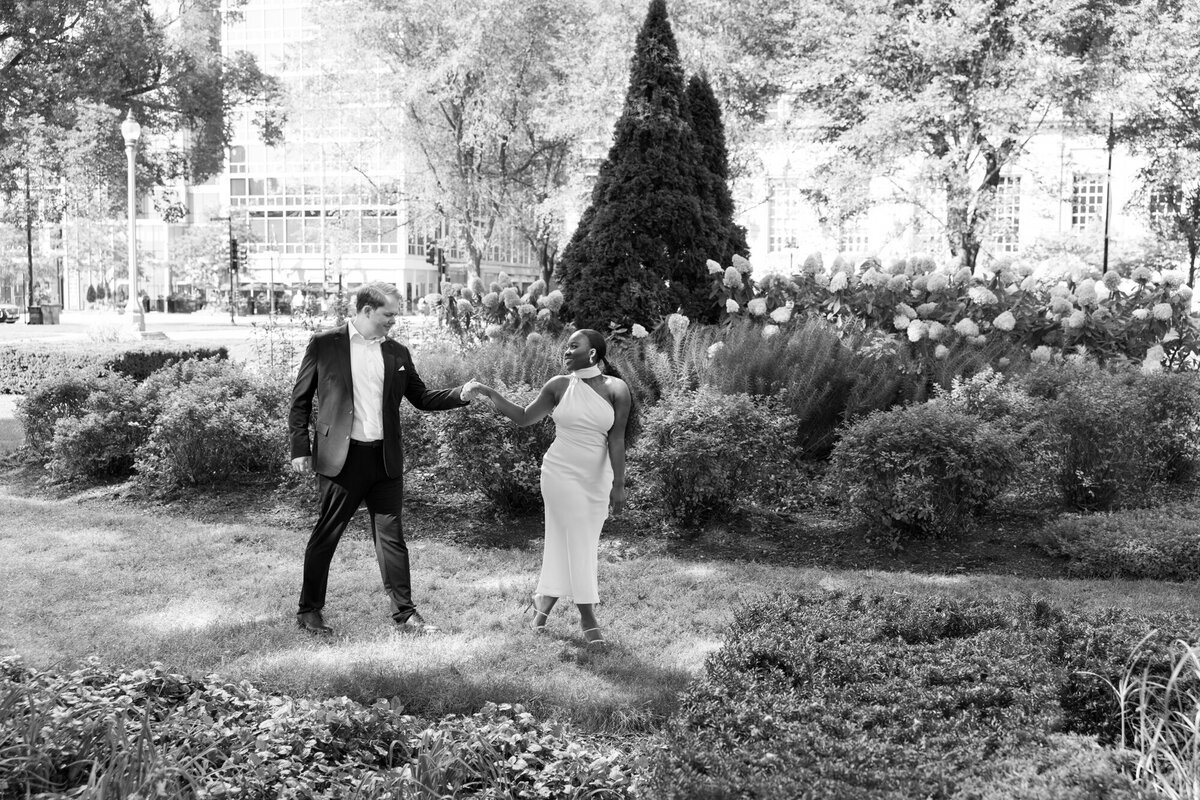 A couple shares a romantic moment in a formal garden along Michigan Avenue, surrounded by lush greenery and city charm.