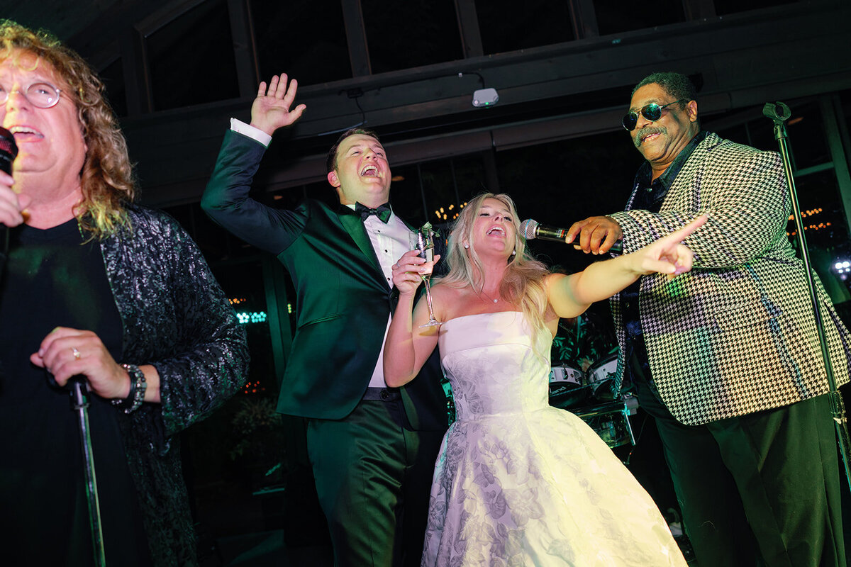 Bride and groom sing and celebrate with a live band on stage during the wedding reception