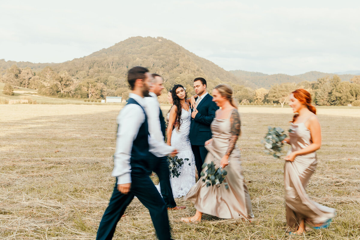 wedding couple standing while wedding party walks in front