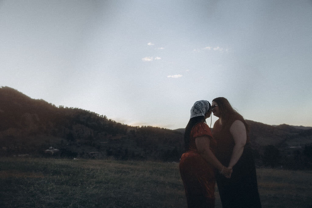 A couple kissing with the sun setting behind them.