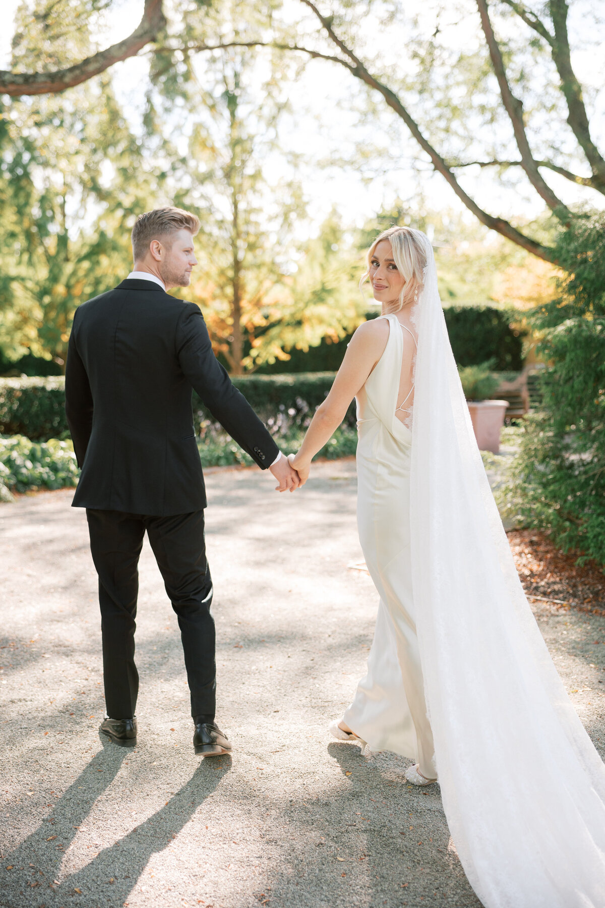 Bride looks over shoulder while holding groom’s hand, outdoor wedding in Dayton, Ohio, by Philadelphia wedding photographer.