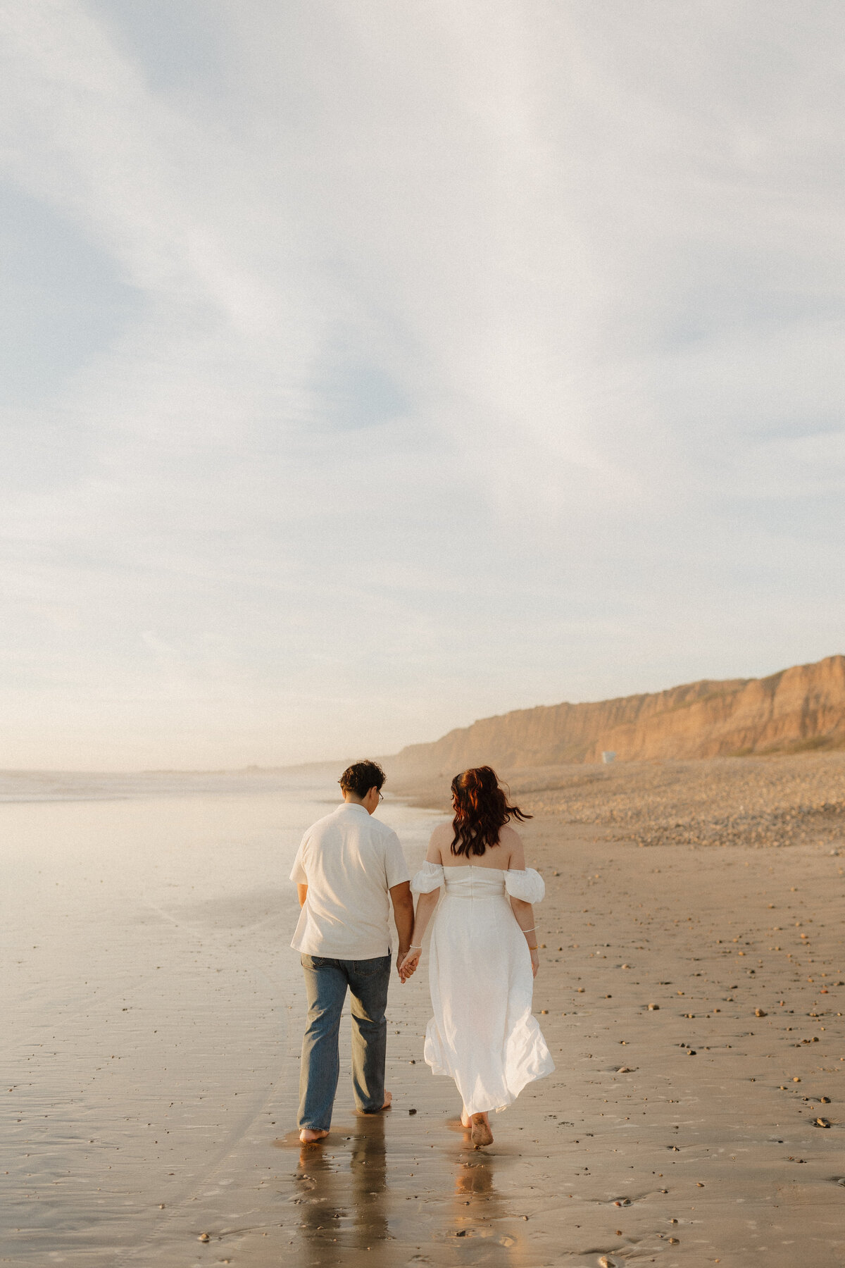 A couple walking on the beach next to the cliffs