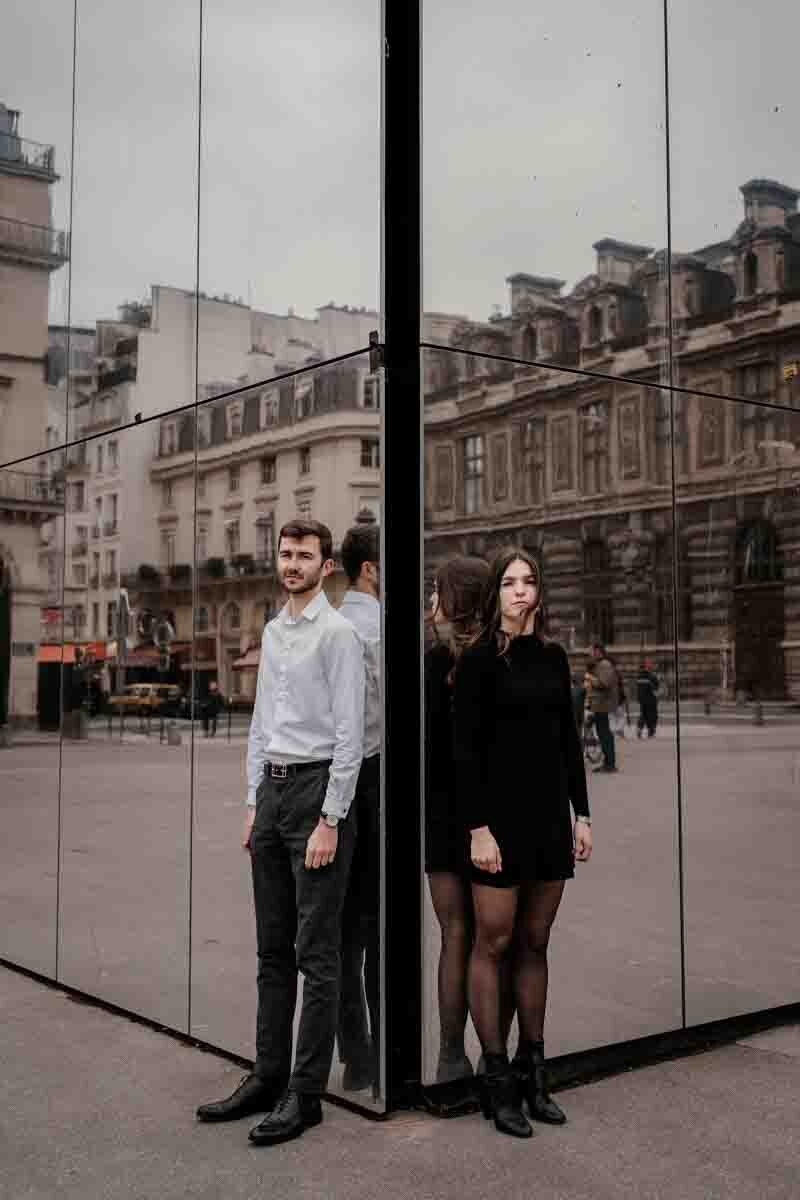 Couple photographié en miroir dans une architecture moderne, ambiance urbaine et graphique près du Louvre.