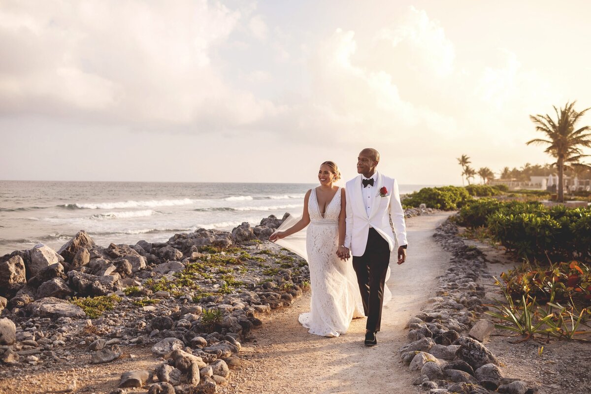 Bride and groom walking on path beside ocean at wedding in Riviera Maya