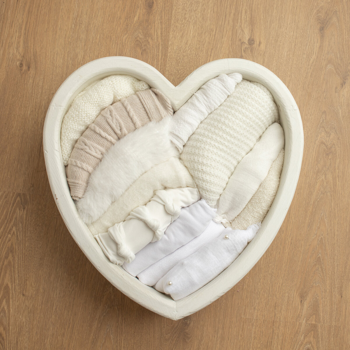 Image is of a heart-shaped newborn photography prop bowl.  The Heart Shaped Bowel contains a number of white and cream coloured wraps for newborn photography . Studio image by Lauren Vanier Photography
