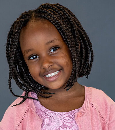 Big smiles from a girl wearing a pink dress and sweater for school portraits.