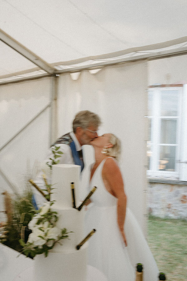 Moment intime entre les mariés qui échangent un baiser sous le chapiteau près du gâteau de mariage. Capturé par Kamesco, photographe vidéaste en Bretagne.