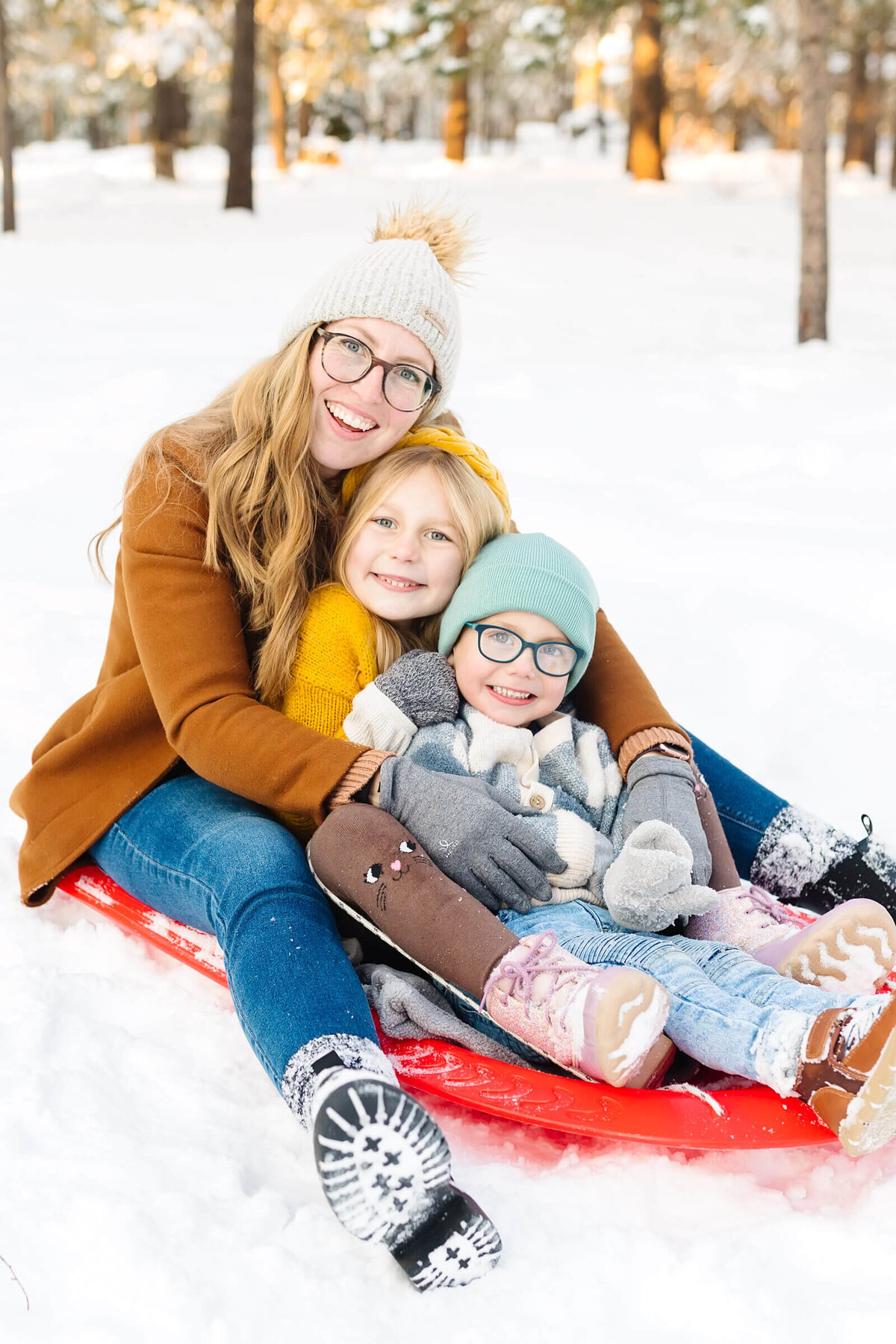 bend-family-photographer-mother-and-children-sitting-on-red-sled-bend-snow-1