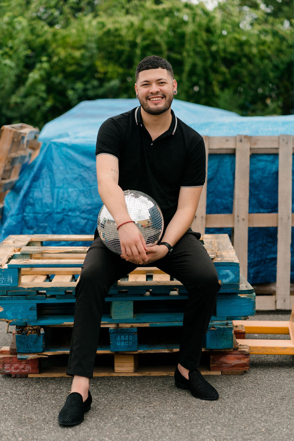 man sitting on a stack of pallets while holding a disco ball