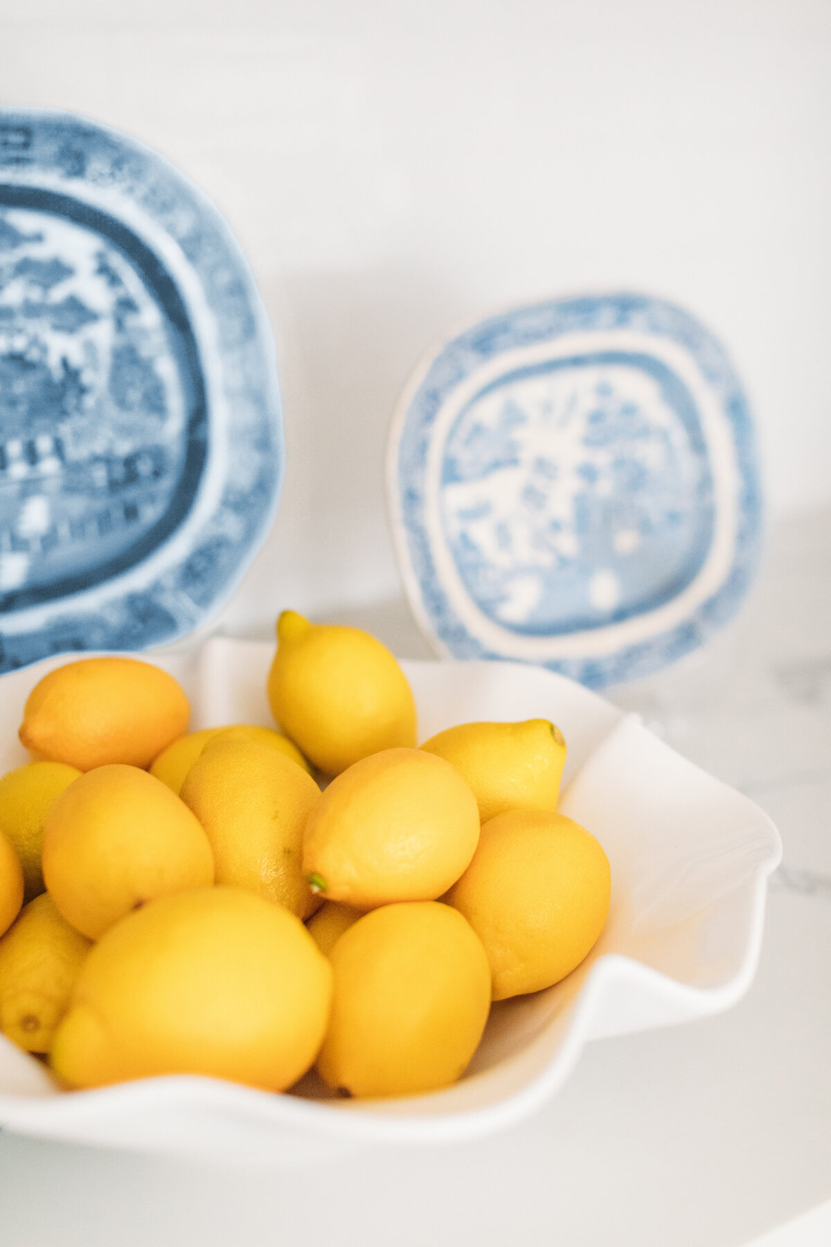 Lemons in a white ruffle fruit bowl and decorative blue and white plates