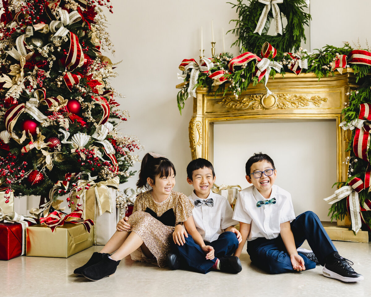 Two boys and one girl sit in front of a Christmas tree in a photography studio in Santa Fe.