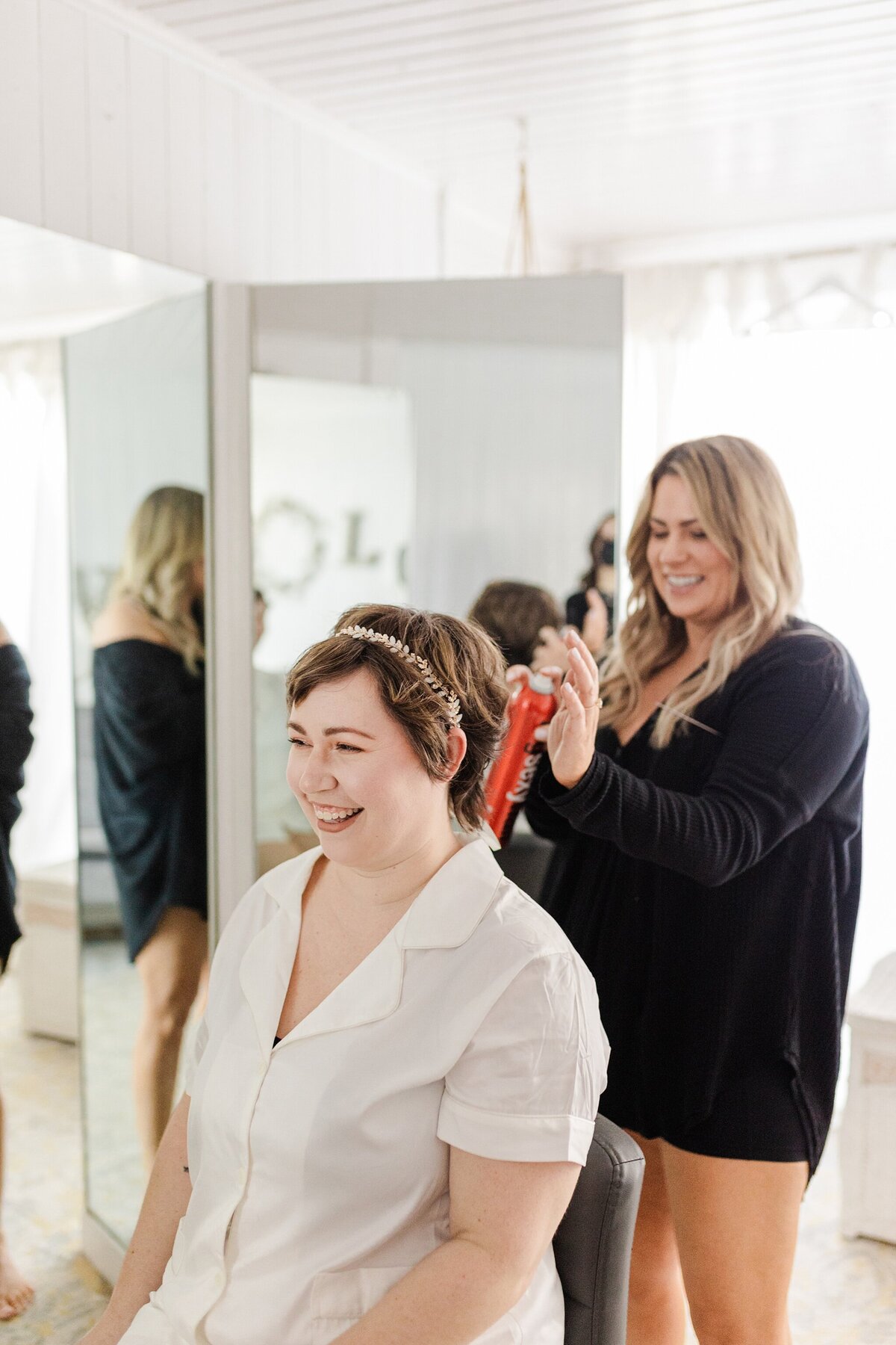 A candid shot of a bride getting her hair done before her wedding ceremony in Dallas, Texas. The bride is wearing a white shirt and a floral headband while her stylist stands behind her wearing all black.