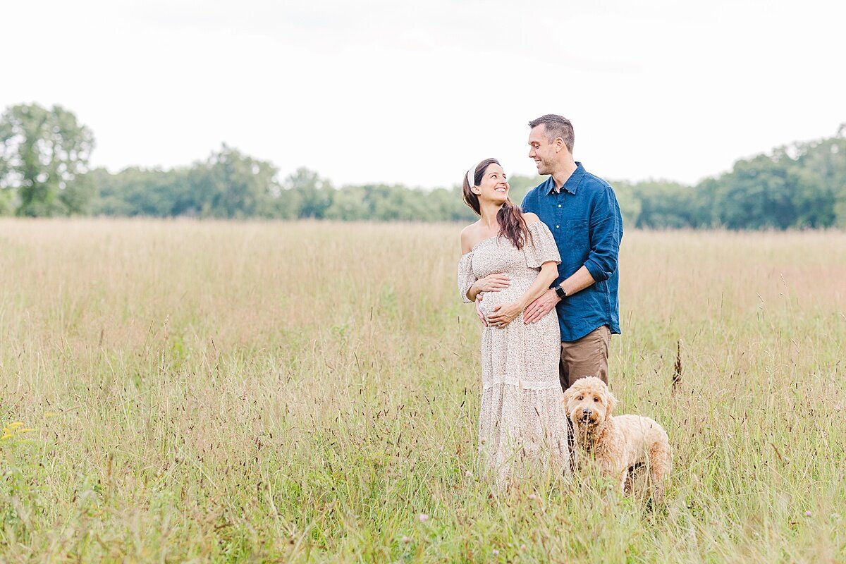 couples stands with dog during maternity photo session with Sara Sniderman Photography at Heard Farm in Wayland Massachusetts