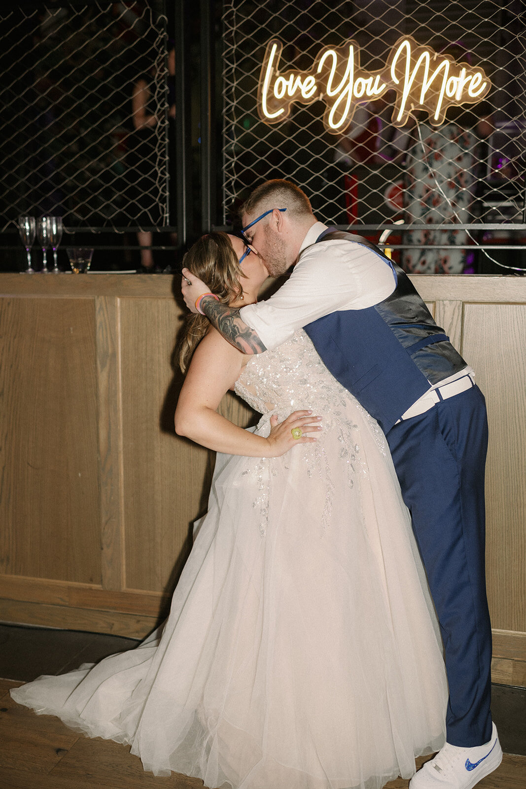 Bride and groom kiss under an I love you more neon sign at their wedding reception at the Rally Hotel in Denver Colorado.