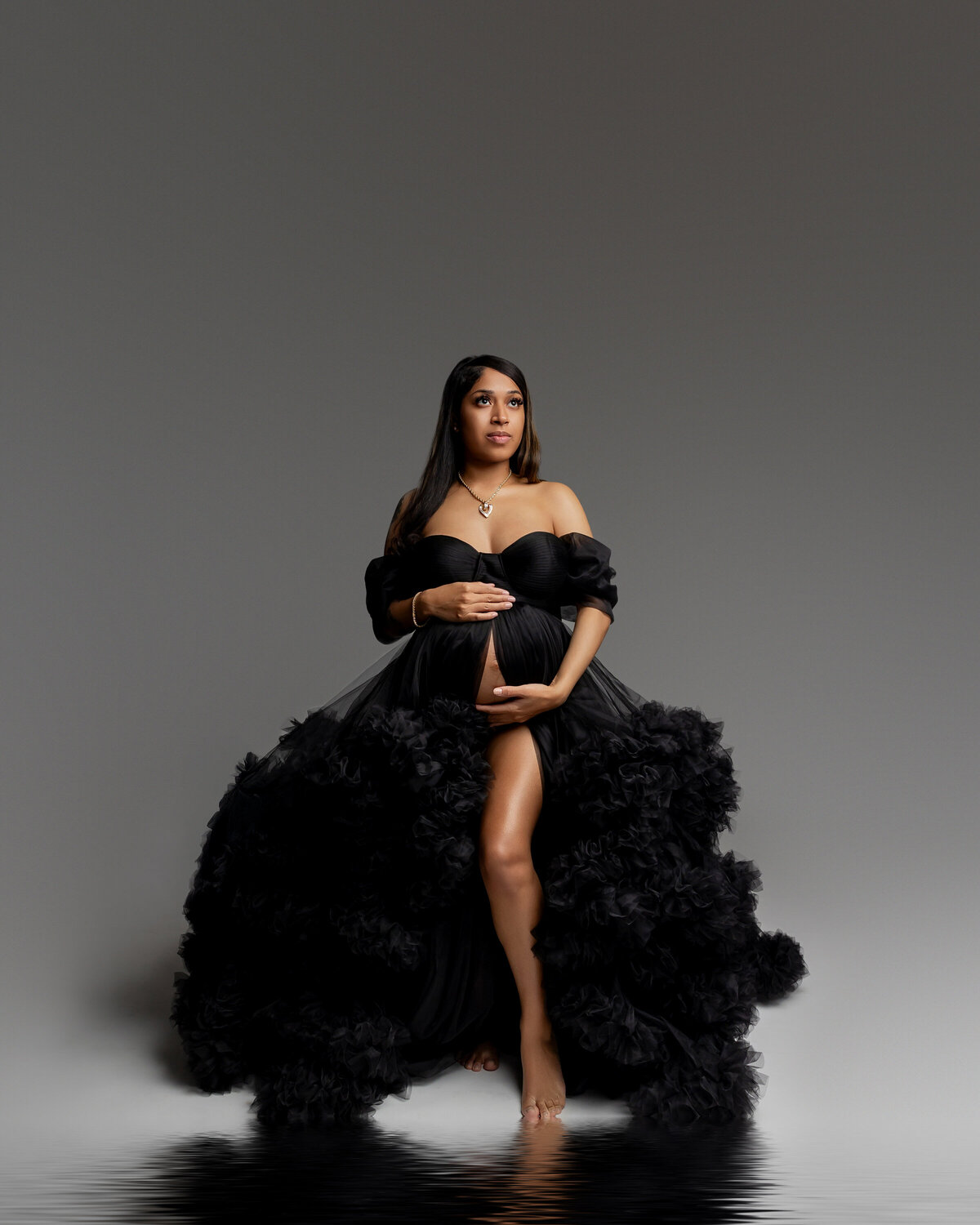Wearing a black dress, the expecting mother lovingly holds her belly, exuding grace and excitement as she prepares for the arrival of her baby. Captured by Inland Empire maternity photographer Kaitlyn Dawn Photography.