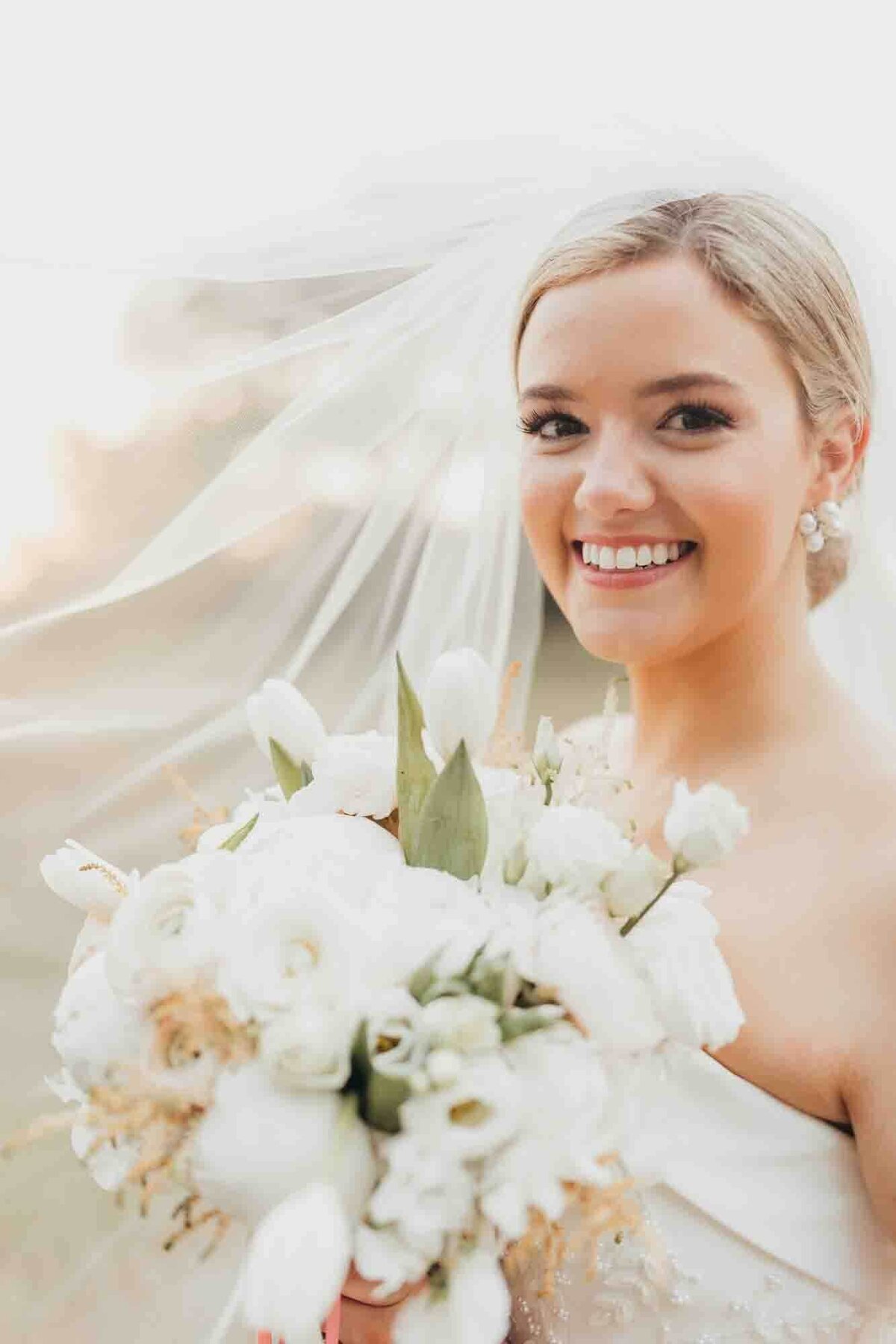 bride smiles while holding her bouquet underneath her veil.