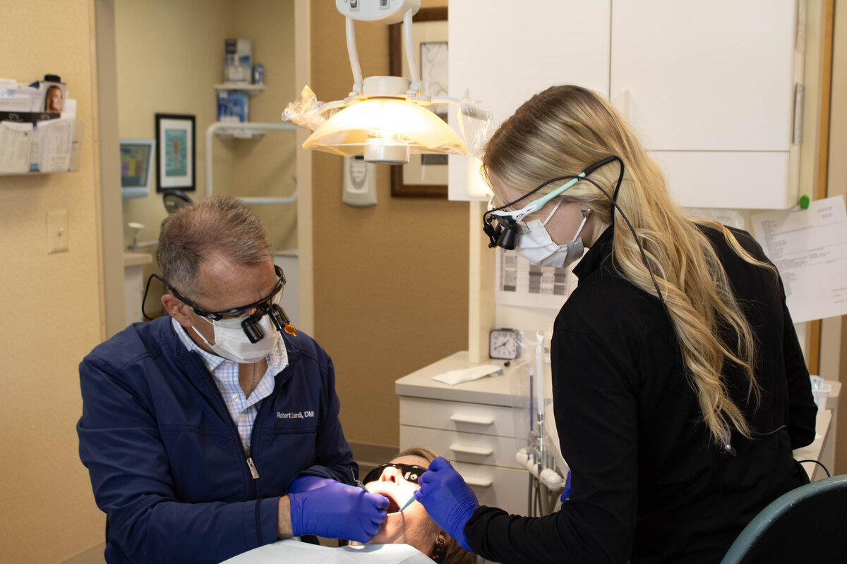 Doctor Leardi reviewing a patients teeth, hygienist nearby offering assistance.