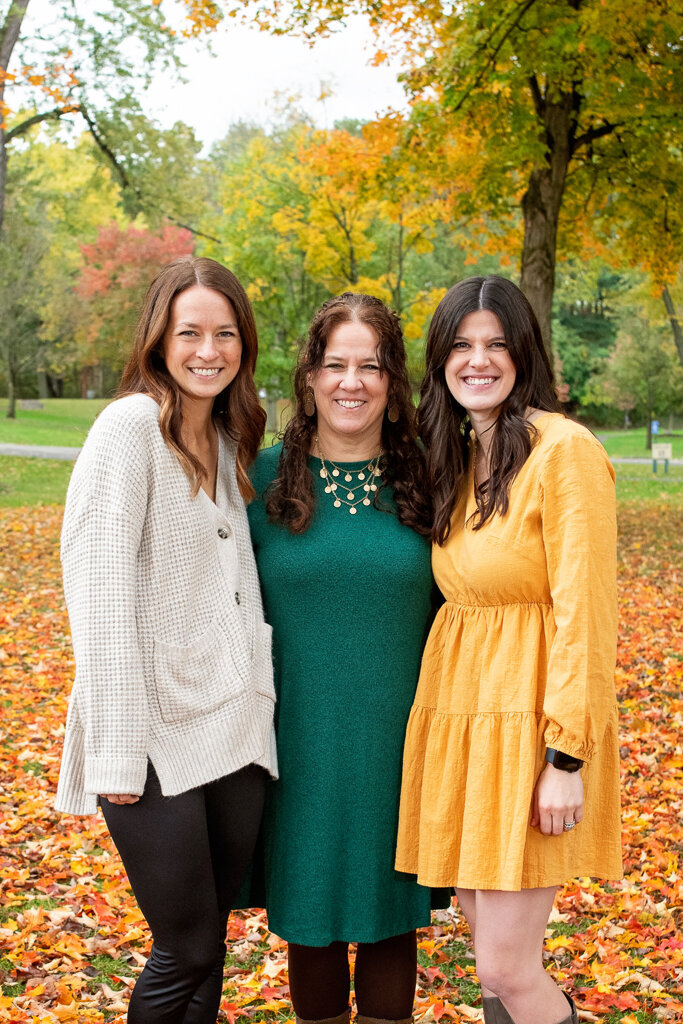 Adult daughters pose with mother in fall leaves