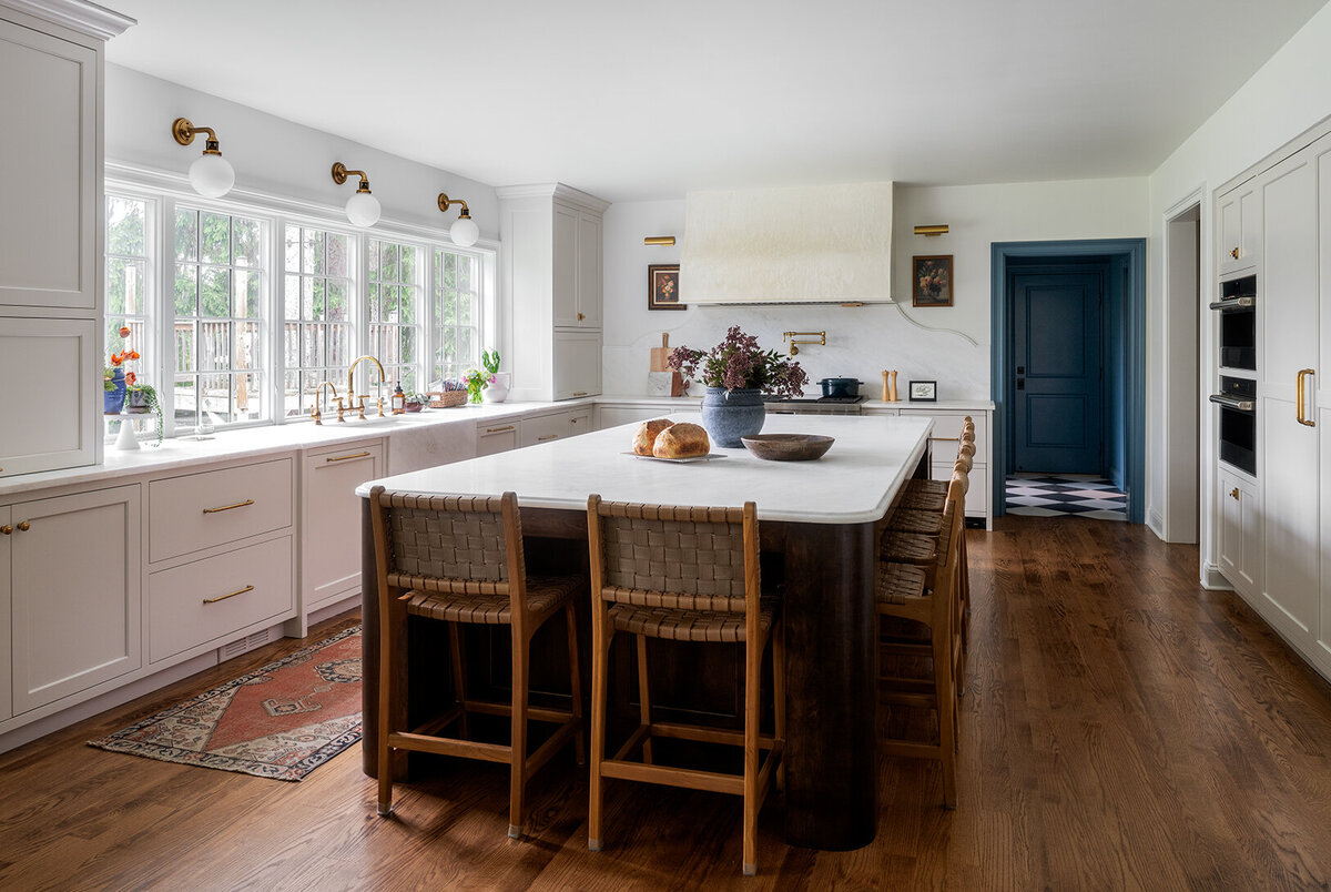 bright white kitchen with large island top and wooden high chairs
