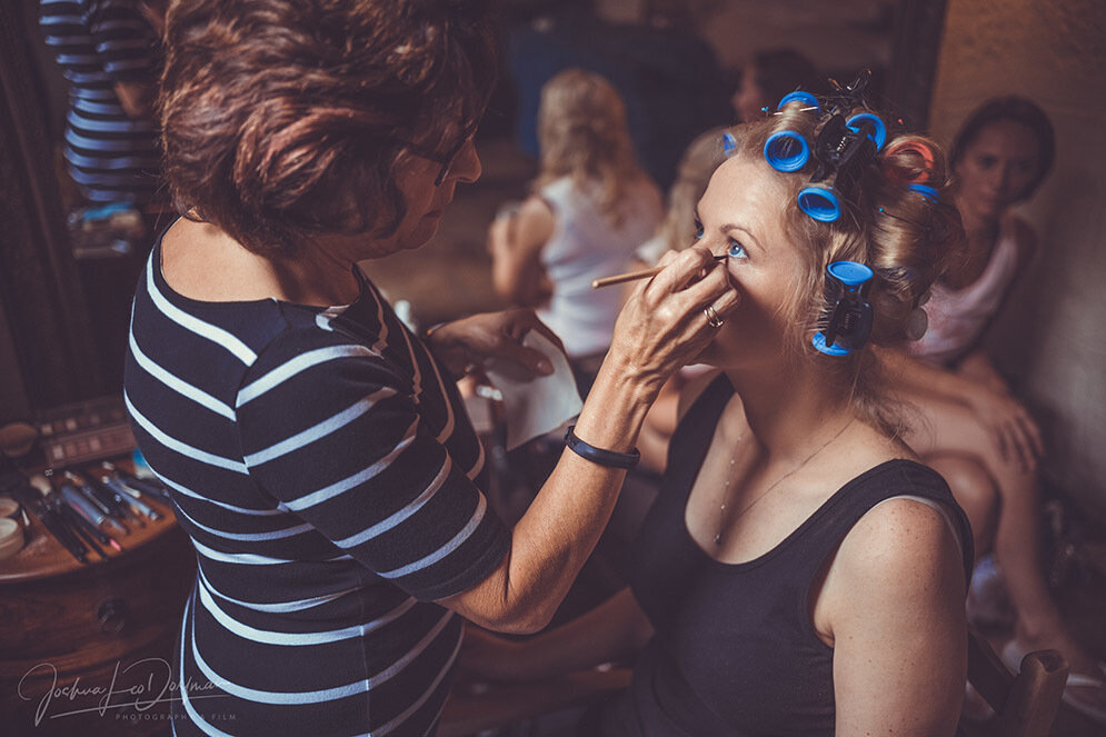 A woman getting her make up done with blue hair rollers