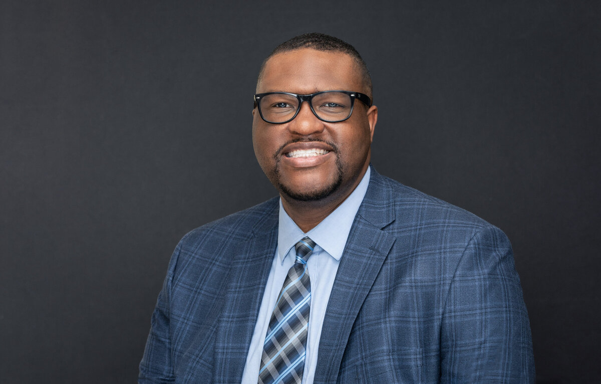 An African American black businessman in a blue suit with glasses poses for a professional headshot photo on location for Janel Lee Photography studios in Cincinnati Ohio