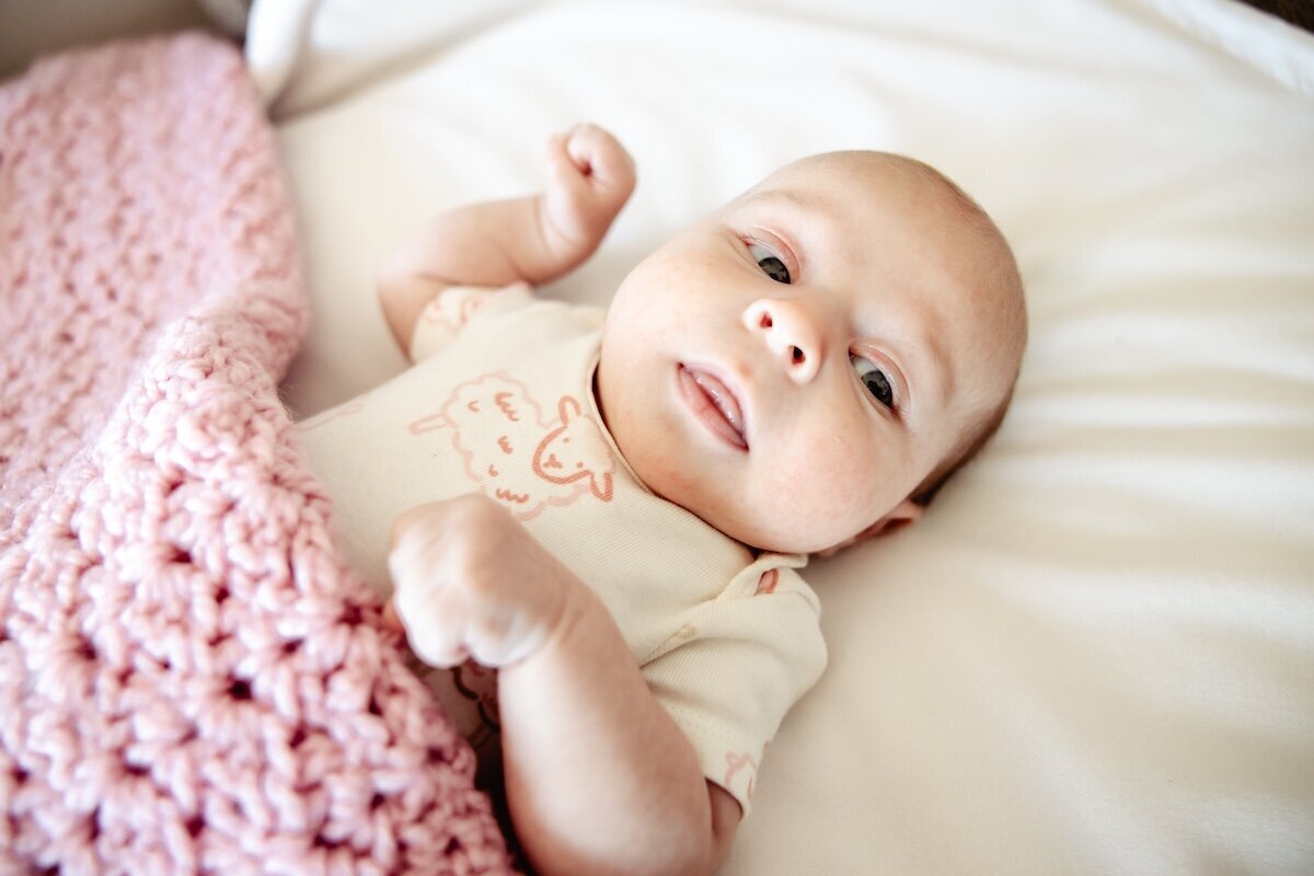 A newborn baby tucked in under a pink knitted blanket 