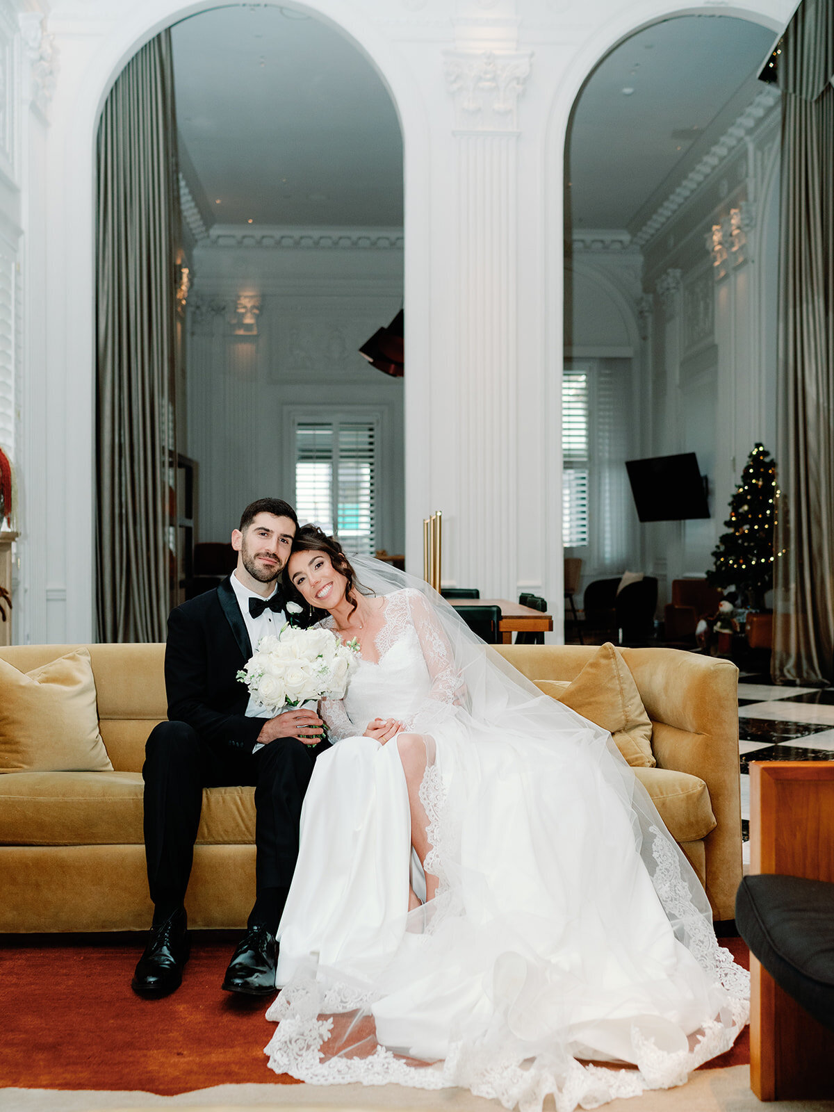 Bride leaning on groom as they sit on a couch at Hotel Washington lobby 