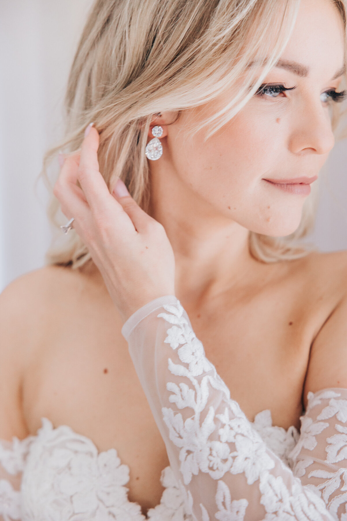 Detail shot of bride putting on gorgeous diamond drop earrings