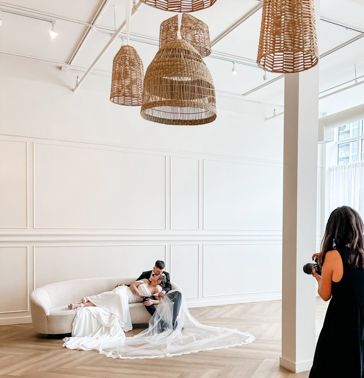 A spacious, modern event venue at Studios at Vic Park in downtown Calgary, featuring large windows with sheer white curtains, herringbone wood flooring, and contemporary furnishings. Bright natural light enhances the elegant and versatile space.