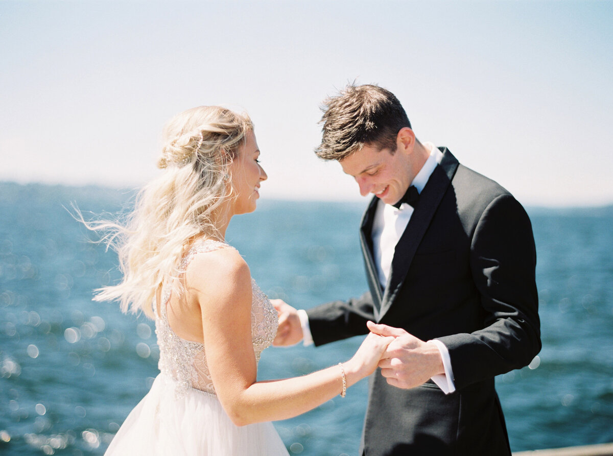 wedding couple hold hands facing one another with blue water in the background