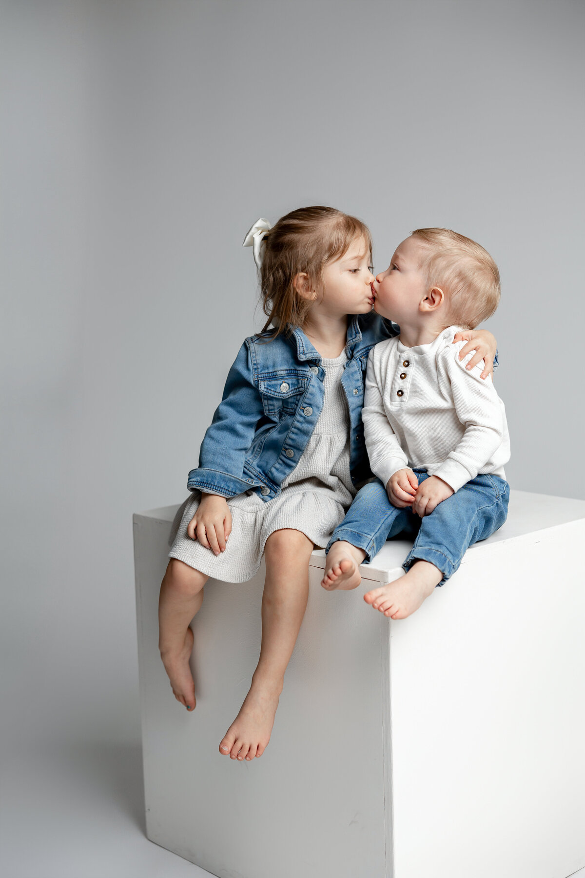 Brother and sister sitting together on cube in denim and neutral outfits, smiling closely. Photographed by Yucaipa family photographer Kaitlyn Dawn Photography.