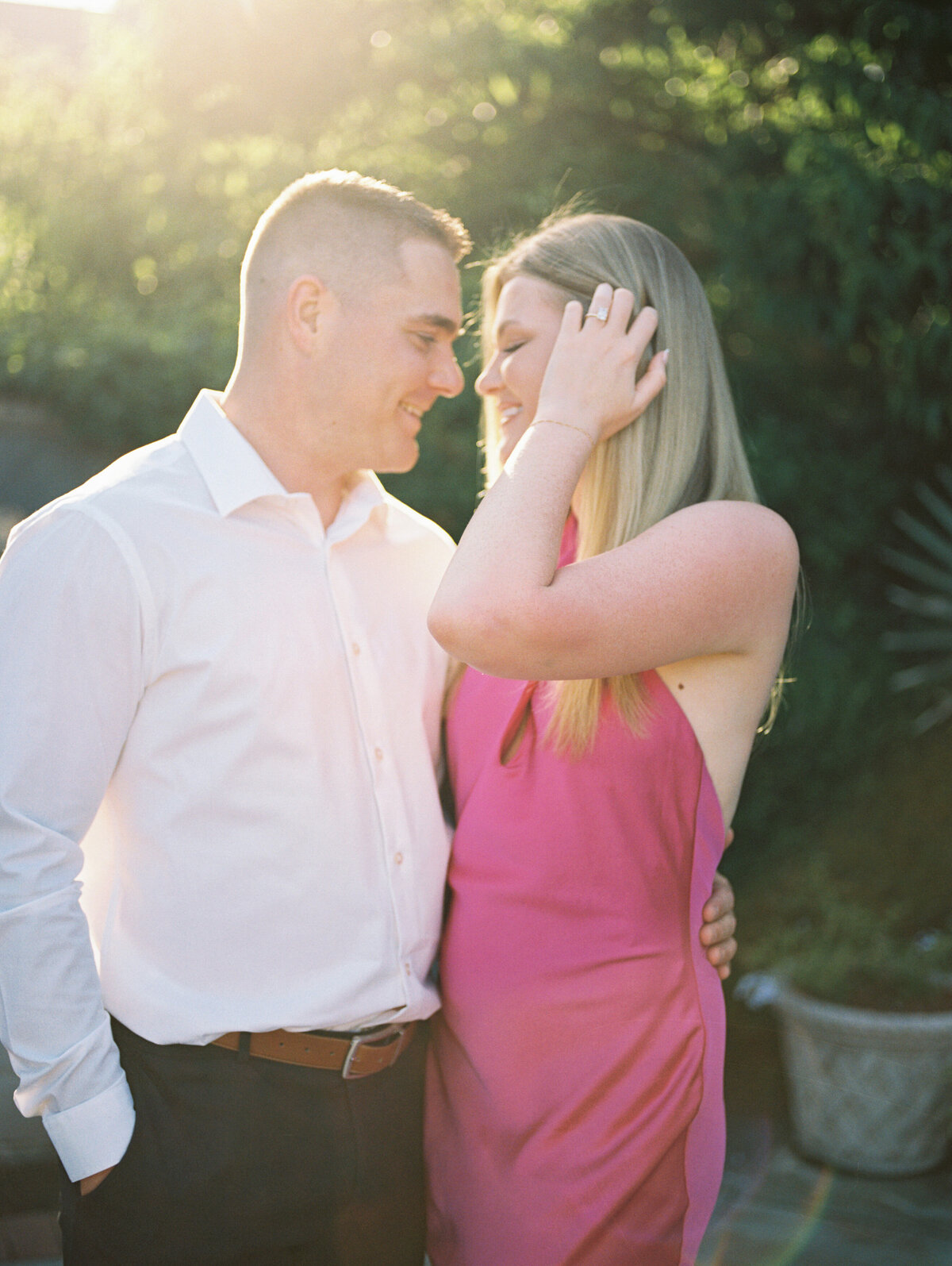 Woman in pink dress adjusts hair while embraced by man in Columbus, Ohio park.