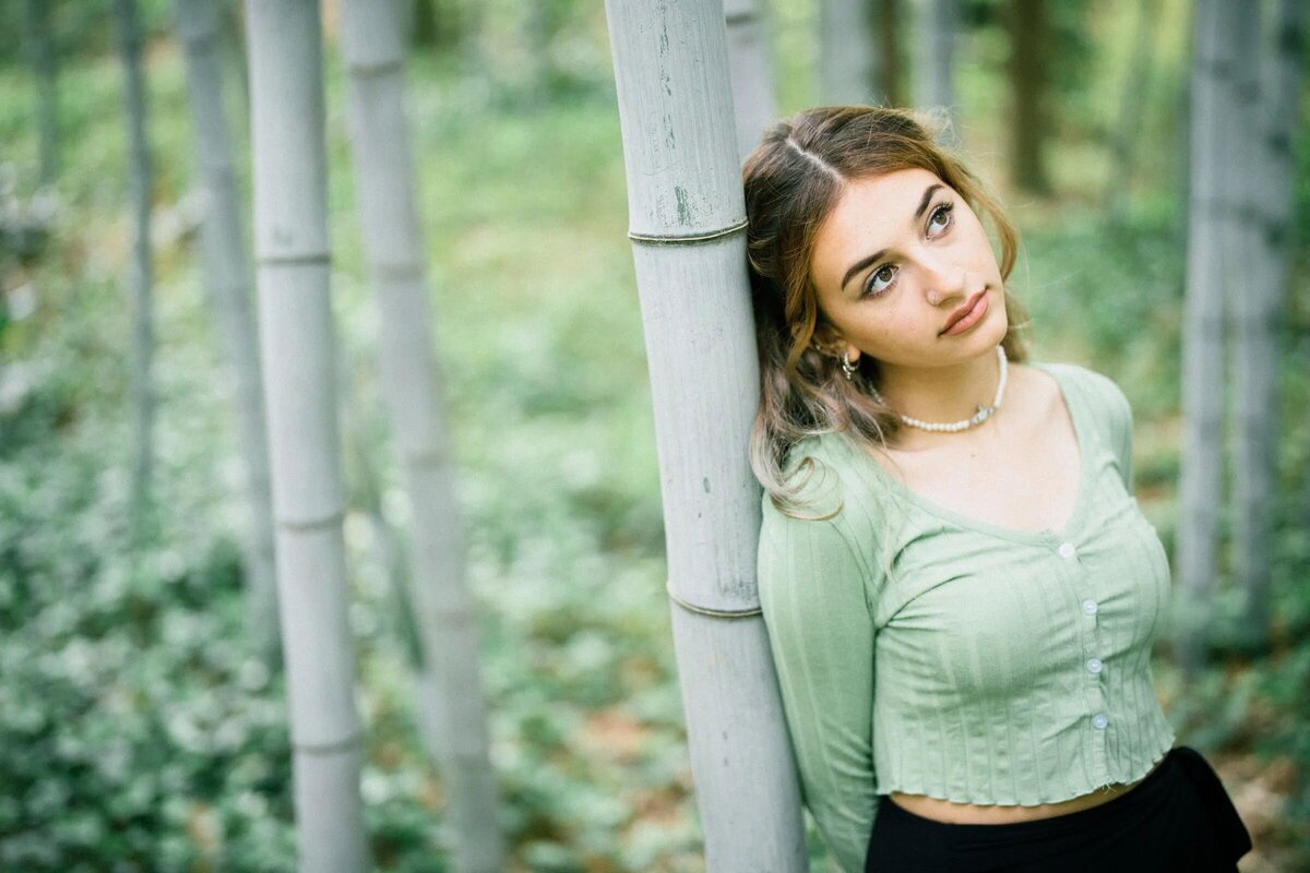 A girl leaning up against a bamboo tree.