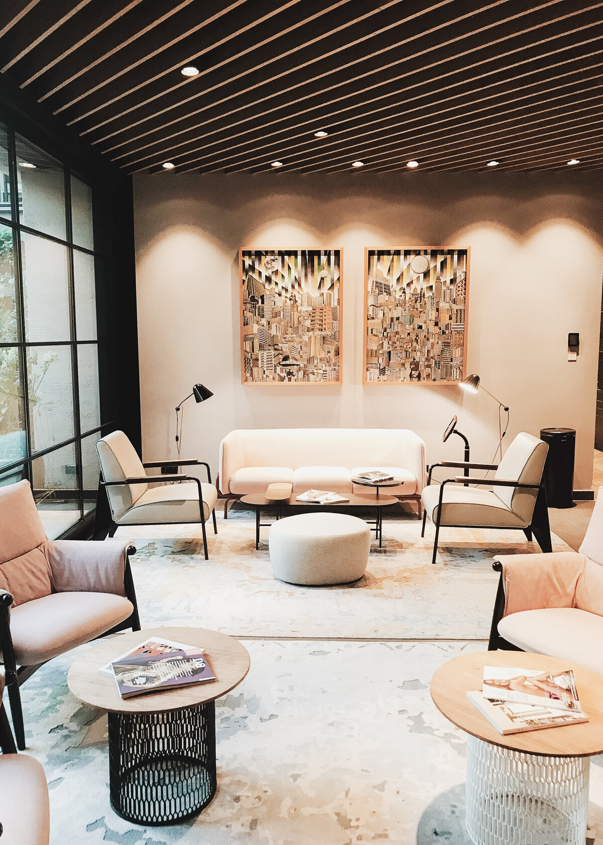 A foyer in a smart office has a with a wooden accent ceiling, stone floor and tan leather seating with black metal detailing.