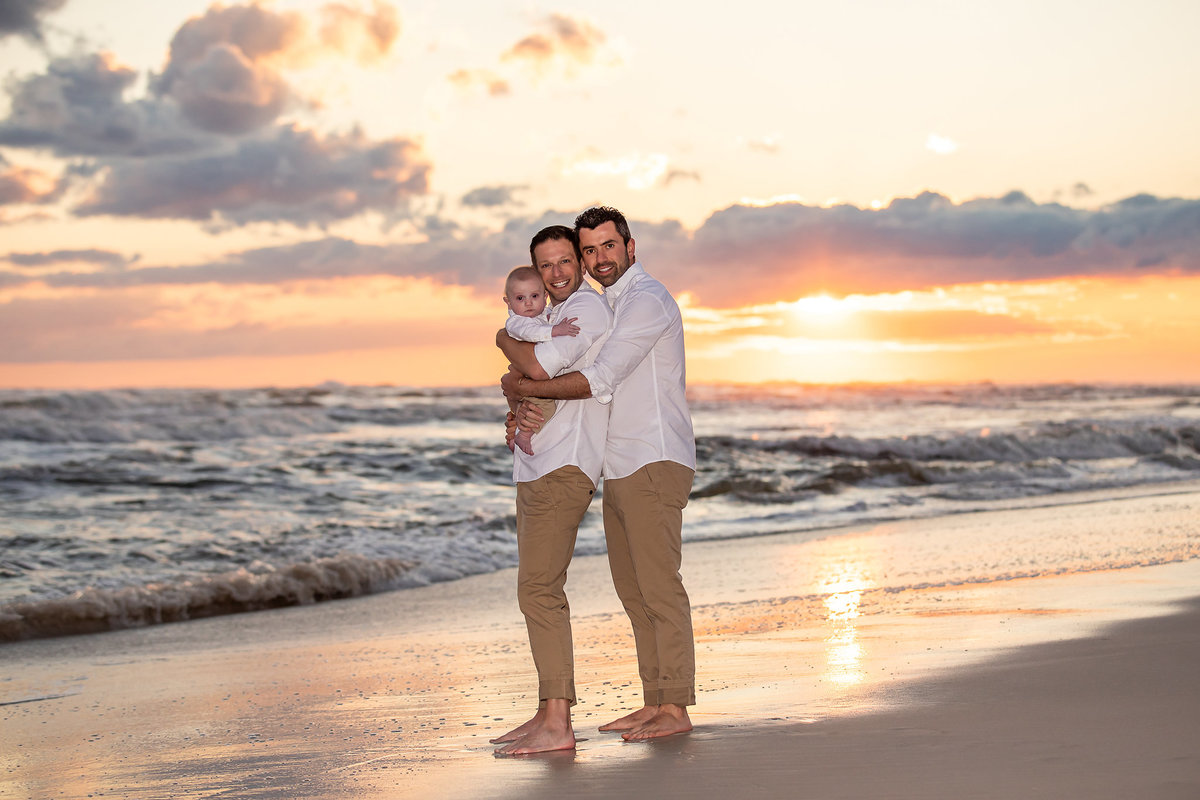 gay men with their new baby on beach with sunset at Alys Beach, Florida.