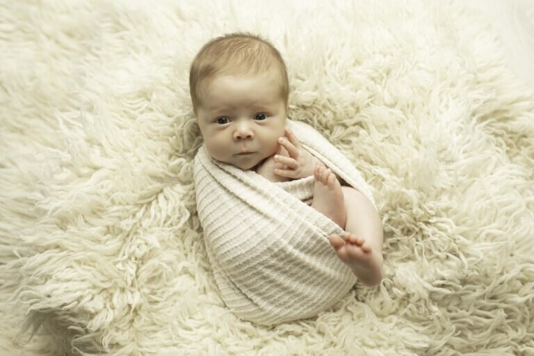 Newborn baby snugly wrapped, gazing curiously with wide-open eyes, capturing a sweet and alert moment in a soft and cozy setting